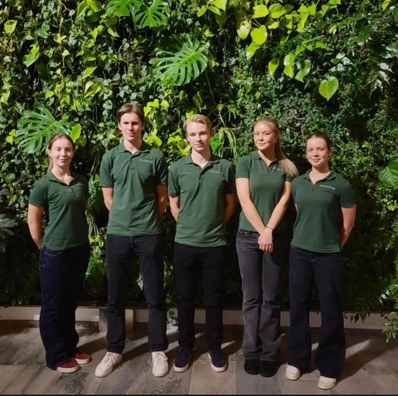 Gruppbild på Collect UF:s fem medlemmar stående framför en grön växtvägg, alla klädda i mörkgröna pikétröjor med företagets logotyp.